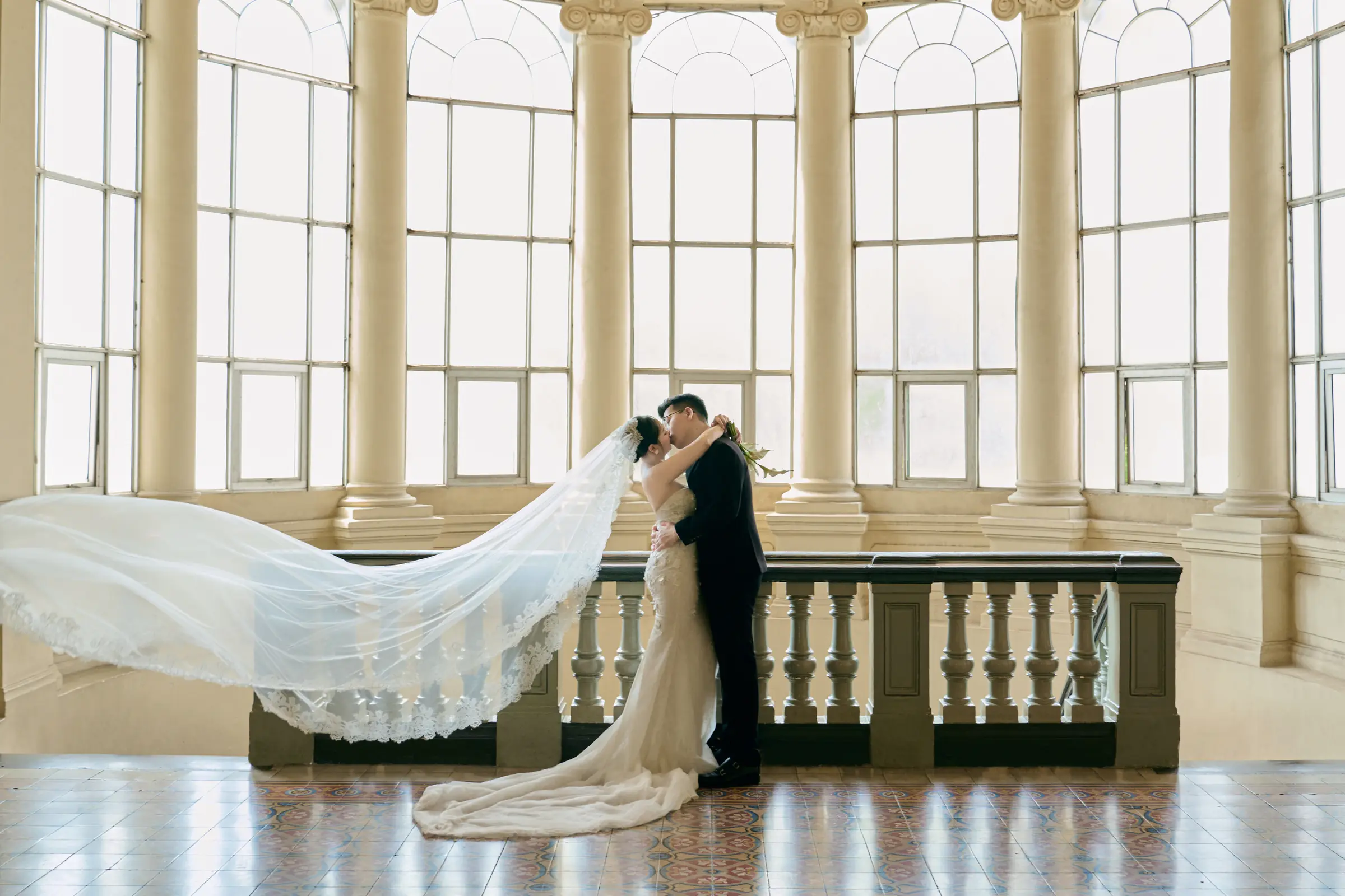 The veil lifted mid-air by the wind as the couple kiss in the rotunda